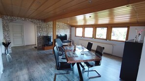 Un coin repas avec une table en bois, des chaises, un téléviseur et un mur en pierre.