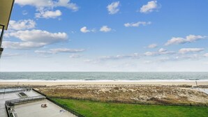 Vista de playa con cielo despejado, arena y zona cubierta de césped con una valla.