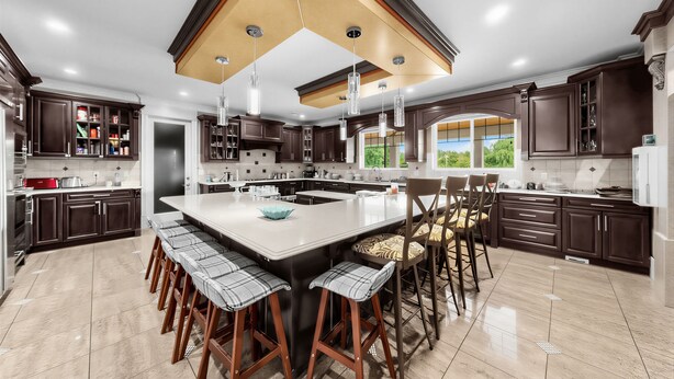 A modern kitchen with dark wood cabinets, a large island with bar stools, and pendant lighting.