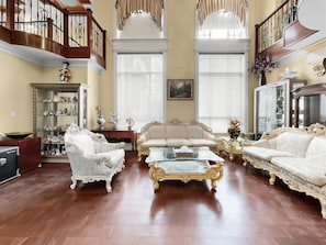 Un vaste salon agrĂ©mentĂ© de meubles Ă©lĂ©gants, dâun magnifique escalier et dâune grande fenĂȘtre dotĂ©e de stores.