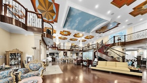 A spacious lobby with a grand staircase, ornate furniture, and a high ceiling with decorative elements.