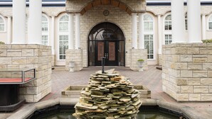 A stone building with a central entrance, columns, and a fountain.
