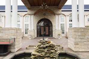 Un bâtiment en pierre doté d’une entrée centrale, de colonnes et d’une fontaine.