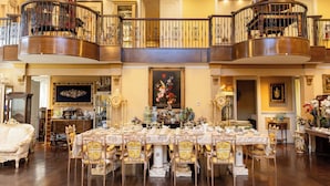 A grand dining room with a large table, ornate chairs, and a staircase with a balustrade.