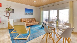 Una sala moderna con un sofá de cuero, una mesa de comedor con sillas, una alfombra azul estampada y un ventanal con vistas.