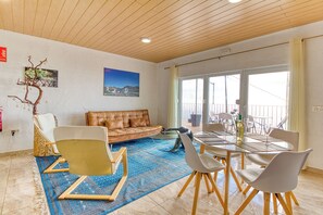Ein modernes Wohnzimmer mit einer Ledersofa, einem Esstisch mit Stühlen, einem blau gemusterten Teppich und einem großen Fenster mit Blick.