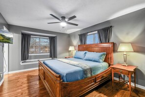 Ein Schlafzimmer mit einem hölzernen Bett, zwei Nachttischlampen, einem Deckenventilator und einem Fenster mit Vorhängen.