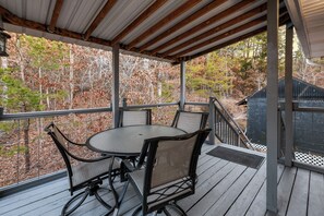 Eine überdachte Terrasse im Freien mit einem runden Tisch und Stühlen, umgeben von einer Holzterrasse und einem Metallgeländer.