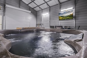 A hot tub in a room with a large window, metal walls, and a flat-screen TV on the wall. - Remote getaway off the parkway- close to everything for 6-8 people! (Sevierville)