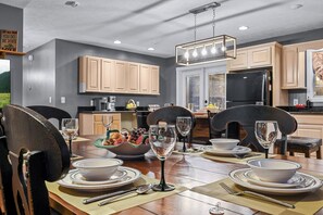A dining area with a wooden table set for four, a bowl of fruit, and wine glasses. - Remote getaway off the parkway- close to everything for 6-8 people! (Sevierville)