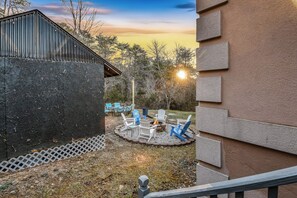 Un patio con mobiliario exterior y una chimenea, rodeado de árboles y un edificio.