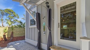 Ein Haus mit überdachter Veranda, einem fenster mit Vorhängen, einer Tür und einer kleinen Sitzgelegenheit im Freien.