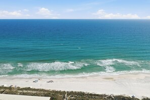 Ein Strand mit Wellen, blauem Himmel und sandigem Ufer.