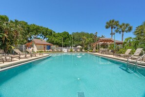 A clear swimming pool with lounge chairs and a covered seating area, surrounded by palm trees and a building with a sign. - Harbor Hideaway|Yard + Community Pool, Near Beach (Palm Harbor)