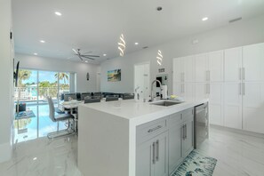 Een moderne keuken met witte kasten, een groot eiland en uitzicht op een zwembad.