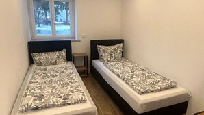 A small, well-lit room with two single beds, a window with a view of trees, and a small table. - Vacation apartment Casita2 ground floor (Essenbach)
