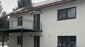 A two-story building with a balcony, a bicycle parked outside, and a small tree in the foreground. - Vacation apartment Casita2 ground floor (Essenbach)