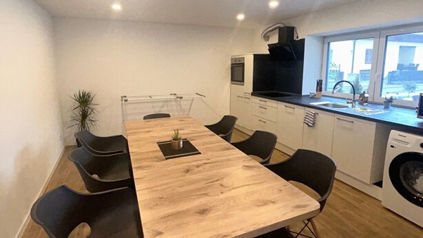 A modern kitchen with a wooden table and chairs, a built-in oven, and a large window. - Vacation apartment Casita2 ground floor (Essenbach)