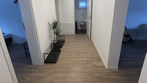 A hallway with a wooden floor, white walls, and a door leading to a bathroom. - Vacation apartment Casita2 ground floor (Essenbach)