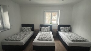 A room with three single beds, a window with a view, and a small table between the beds. - Vacation apartment Casita2 ground floor (Essenbach)