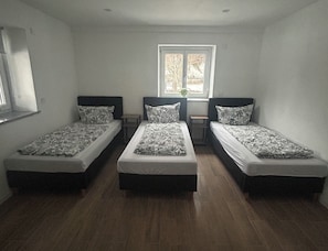 A room with three single beds, a window with a view, and a small table between the beds.