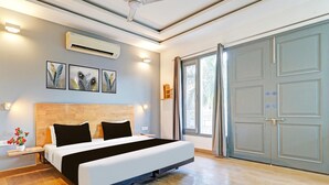 Een moderne hotelkamer met een groot bed, een airconditioner, een kunstwerk aan de muur, een nachtkastje met een vaas en een glazen schuifdeur.