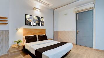 A modern hotel room with a wooden headboard, a large bed, a nightstand with a plant, and a door with a handle.