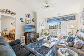 A living room with a sofa, armchair, and coffee table, a television, decorative wall art, and a ceiling fan. - Golf Getaway- Pools- Near Beach! (Longs)