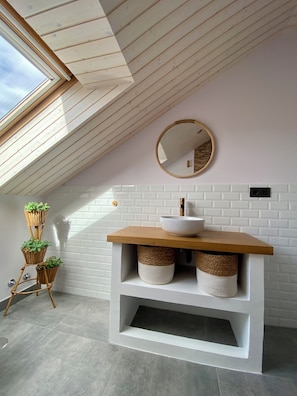 Een moderne badkamer met dakraam, een ronde spiegel, een witte wastafel en rieten manden.