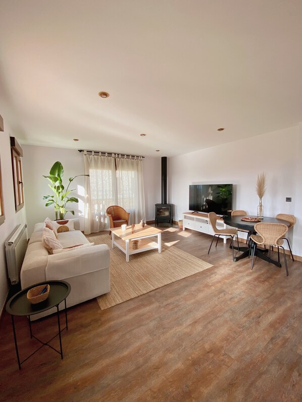 Un salon comprenant un canapé, une table basse, un téléviseur, une cheminée, une table à manger, des chaises et une plante en pot.