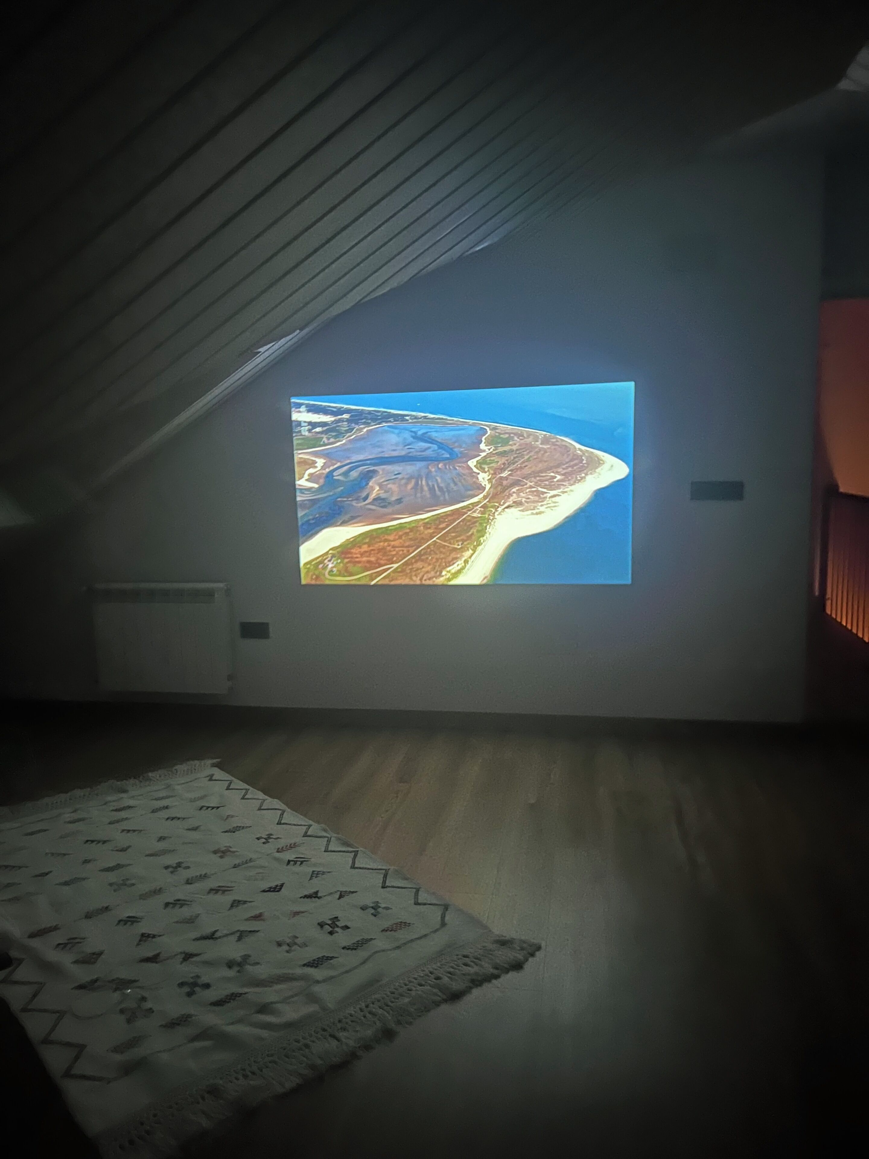 A room with a projection screen displaying an aerial view of a coastal area.