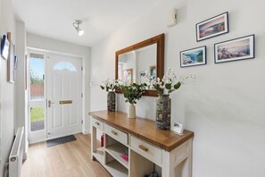 A hallway with a white door, a wooden console table with vases, a mirror, and framed pictures on the wall. - NEW!4BR Ideal for Contractors, Driveway, Wifi, M40 (Heathcote)