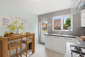 Una cocina moderna con armarios blancos, estufa a gas y ventana con vista a una zona residencial.