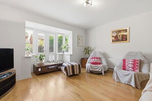 A living room with a TV, a sofa, a chair, a window, and a painting on the wall. - NEW! 4BR Ideal for Contractors, Driveway, Wifi, M40 (Heathcote)