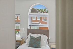 Un dormitorio con cama, mesita de noche, lámpara y ventana con persianas.