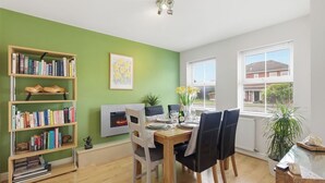 Uma sala de jantar com mesa de madeira, cadeiras, estante, lareira e janela com persianas.