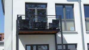 A modern building with a balcony, large windows, and a sign indicating a residential area. - Ferienwohnung in Orth auf Fehmarn (Fehmarn)