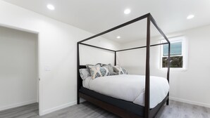 Un lit à baldaquin avec une structure sombre, un matelas blanc et des oreillers à motifs.
