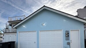 Un bâtiment de couleur bleu clair, doté de deux portes de garage blanches, d’un petit balcon avec des balustrades et d’une allée en béton.