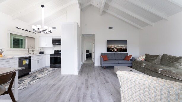 Un intérieur moderne comprenant une cuisine, un coin repas et un espace de vie, avec des meubles blancs, un canapé gris et une vue sur la ville.
