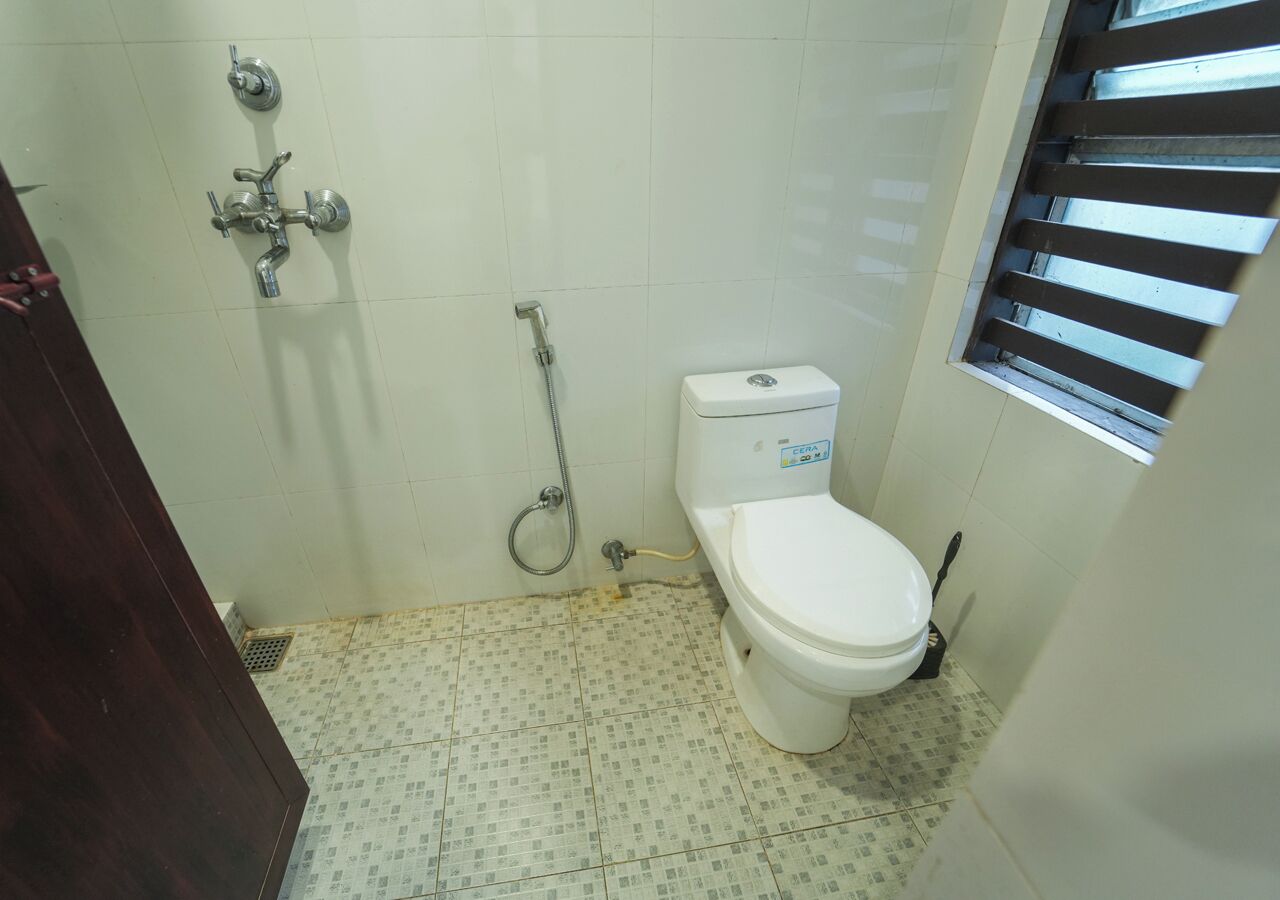 A small bathroom with a toilet, a shower, and a window with blinds.