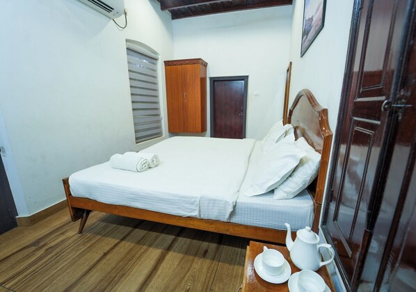 Un dormitorio con una cama de madera, un armario, una puerta y una mesita con una tetera y tazas.