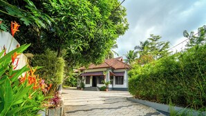 A house with a tiled pathway leading to the entrance, surrounded by lush greenery and a variety of plants. - POP Tavern Pool Villa by VOYE HOMES (Kovalam)