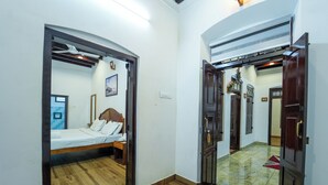 A bedroom with a bed, a nightstand, a wooden floor, and a door leading to another room. - POP Tavern Pool Villa by VOYE HOMES (Kovalam)