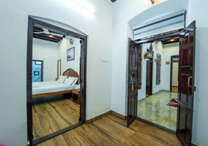 Une chambre à coucher avec un lit, une table de chevet, un plancher en bois et une porte donnant sur une autre pièce.