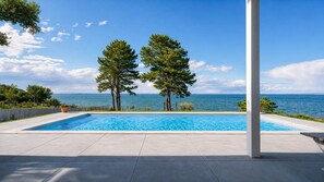 Ein Swimmingpool mit Meerblick, zwei Bäume und ein klarer Himmel.