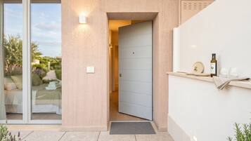 Ingresso di un edificio moderno con porta scorrevole in vetro che conduce a una camera da letto, una porta azzurra e un piccolo spazio all'aperto con una bottiglia e dei bicchieri.