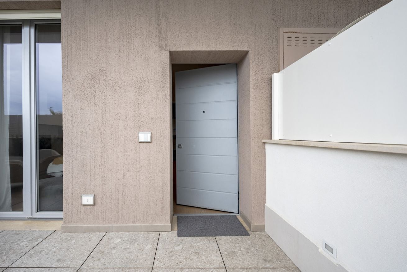 Ingresso di un edificio moderno con una porta scorrevole in vetro, un muro in cemento e una porta di azzurro chiaro.