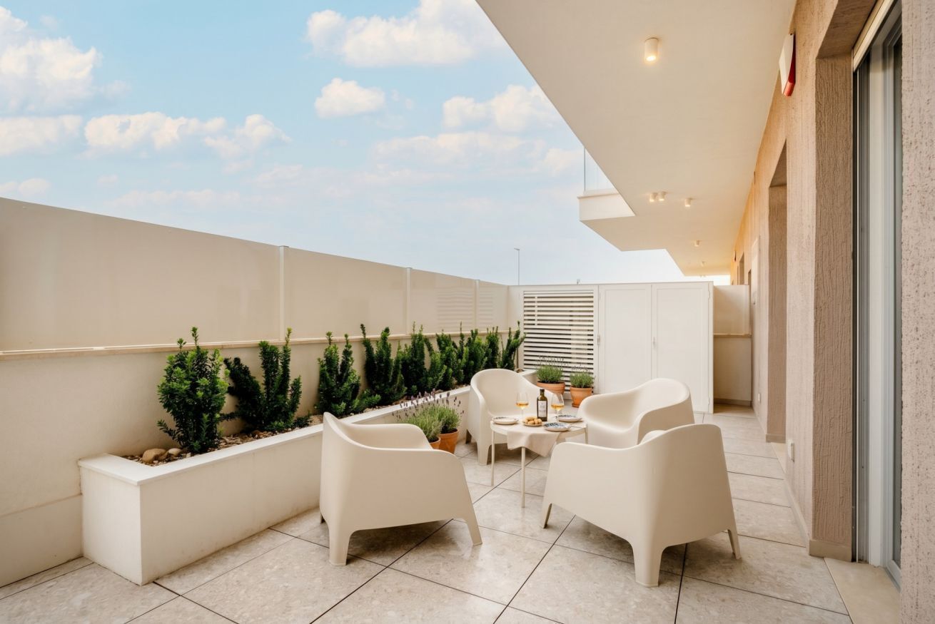 Une terrasse extérieure moderne, avec des meubles blancs, des plantes en pot et une vue dégagée sur le ciel.