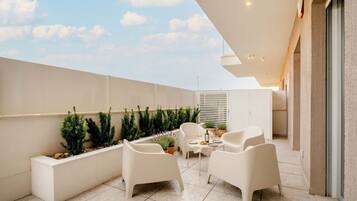 Une terrasse extérieure moderne, avec des meubles blancs, des plantes en pot et une vue dégagée sur le ciel.